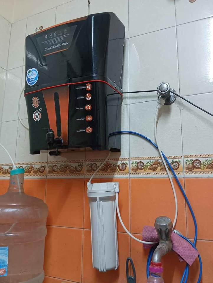 Aqua D Pure Copper + Alk RO wall mounted installation with inlet and reject water lines, showing rejected RO wastewater being collected in a jar for safe reuse or disposal