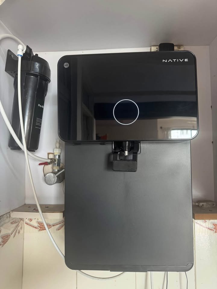 Close-up of UC Native M1 RO under-sink water installation showing pre-filter housing, tubing, and inlet valve connection